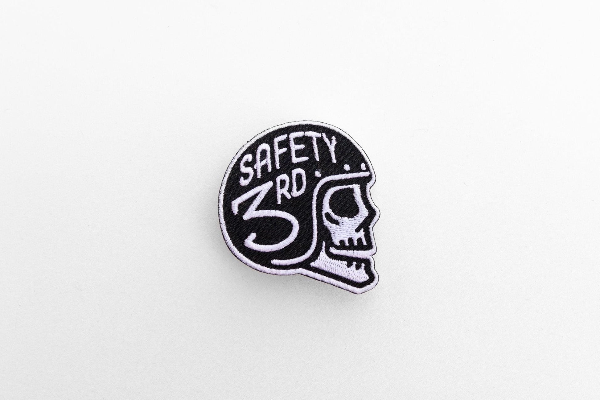 Small against a wide white background, the Safety 3rd Helmet Patch sits alone with its skull facing right.