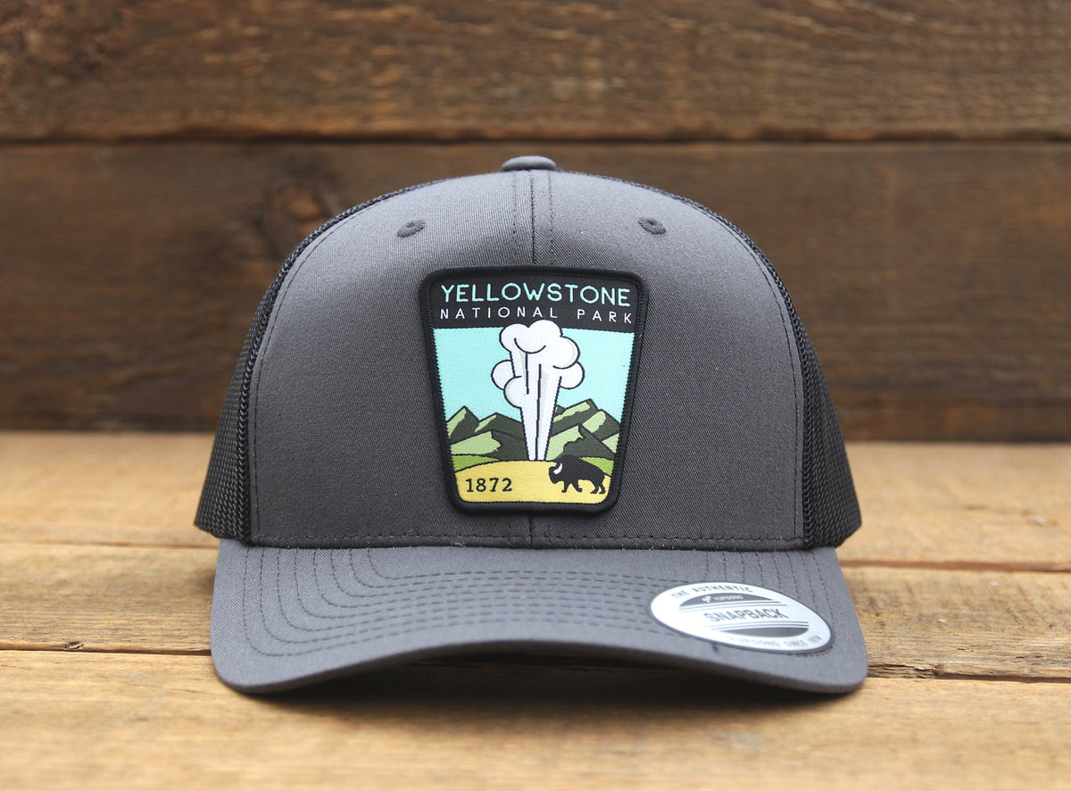 Charcoal and black Yellowstone National Park trucker hat resting flat, brim label still on the front edge.