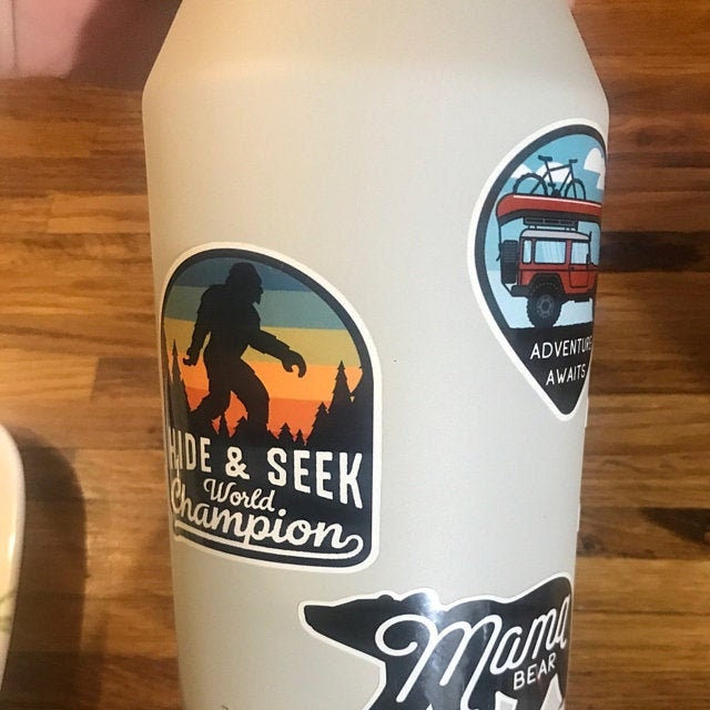 A tan water bottle carries the Bigfoot Hide & Seek World Champion sticker beside a van and a bear decal.