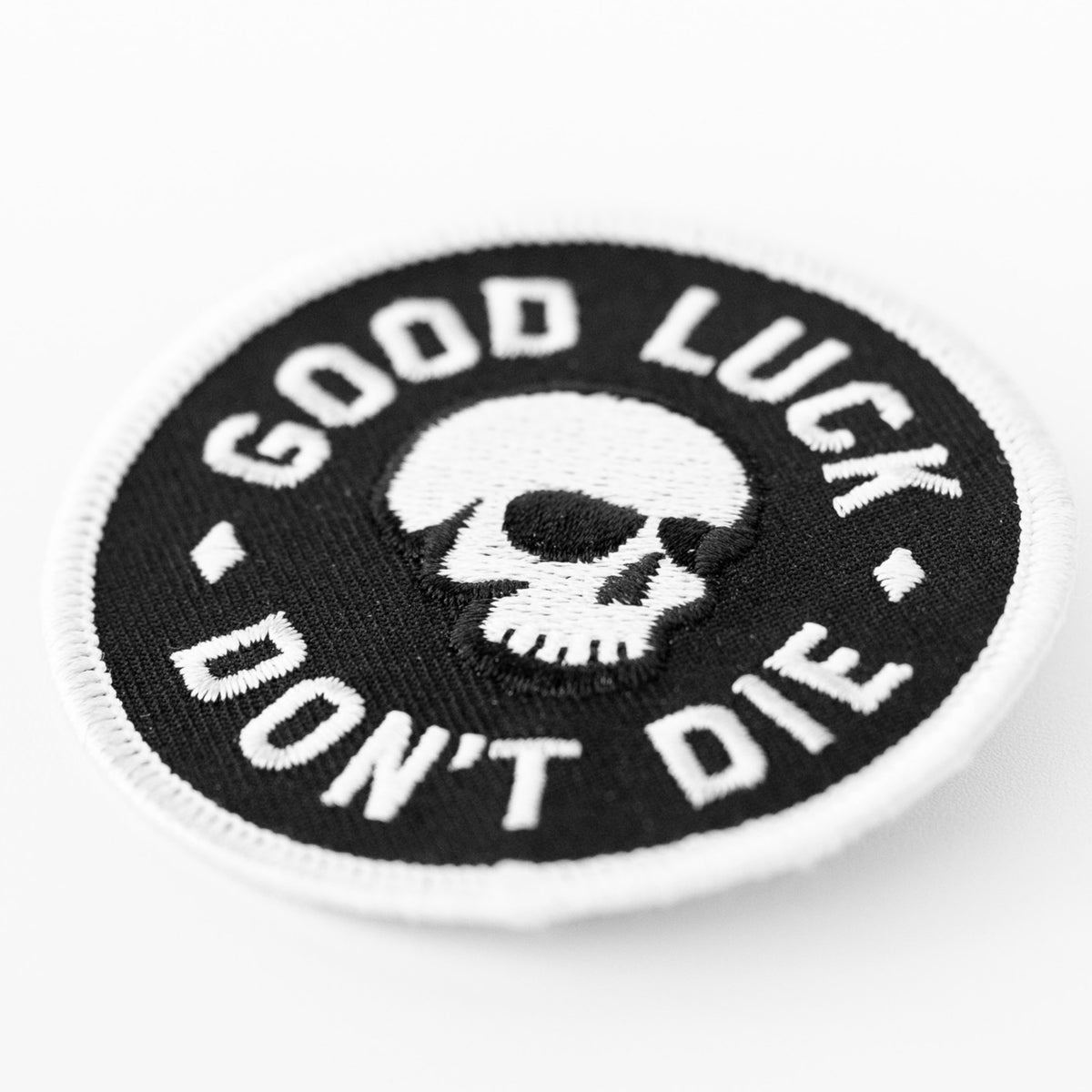 Tilted close up view shows the Good Luck Don't Die patch with its round white border and skull embroidery.