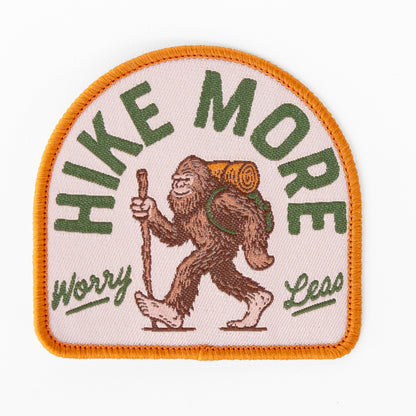 Flat against a white background, the Hike More Worry Less patch shows Bigfoot walking with a backpack and hiking stick.