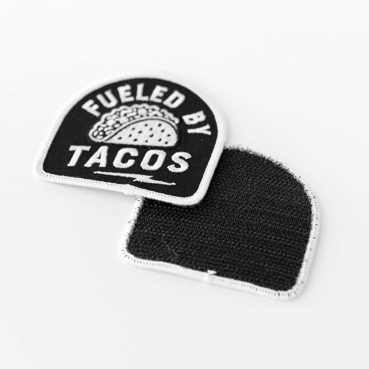 Flipped to show both sides, the Fueled By Tacos patch reveals its black fabric backing next to the stitched front.