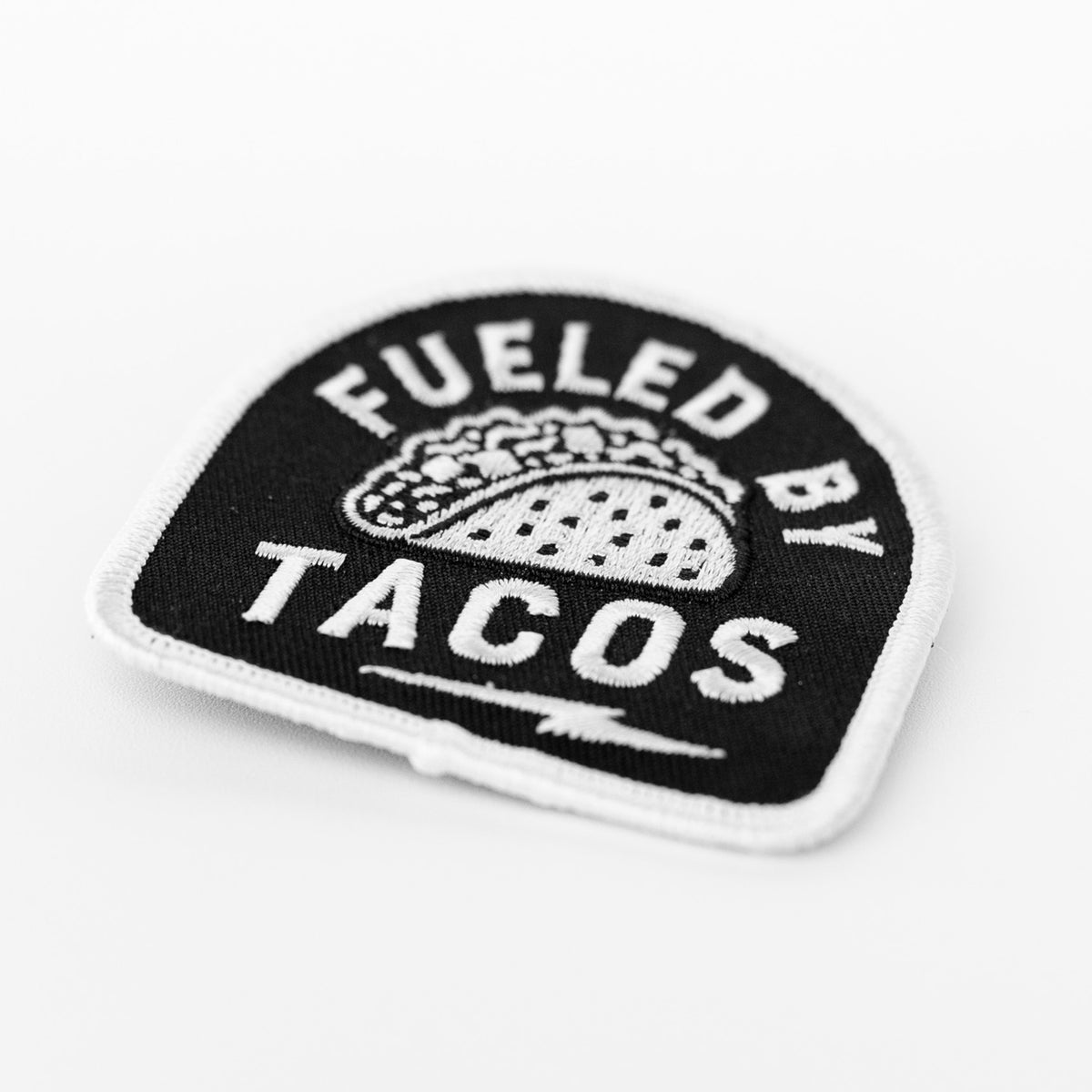 Tilted at an angle, the Fueled By Tacos patch catches the light across its white embroidered border.