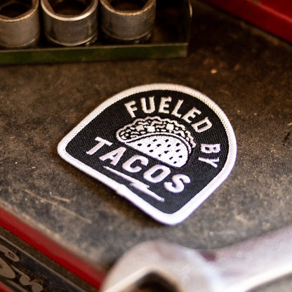 Resting on a grimy red toolbox beside sockets and a wrench, the Fueled By Tacos patch sits near a Snap-on logo.