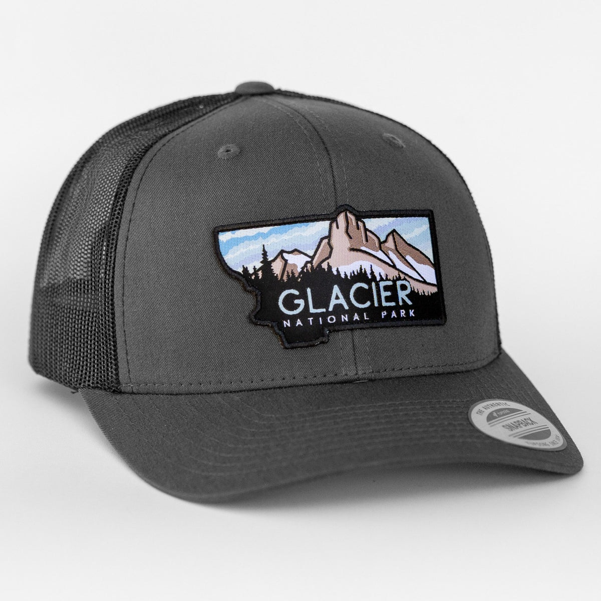 A charcoal Glacier National Park trucker hat displays its mountain patch against matching black mesh panels.