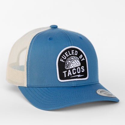 Blue twill and cream mesh make up this Fueled By Tacos trucker hat, patch stitched above a curved brim.