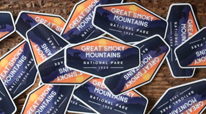 A scattered pile of Smoky Mountains National Park stickers covers a worn brick surface, edges overlapping.