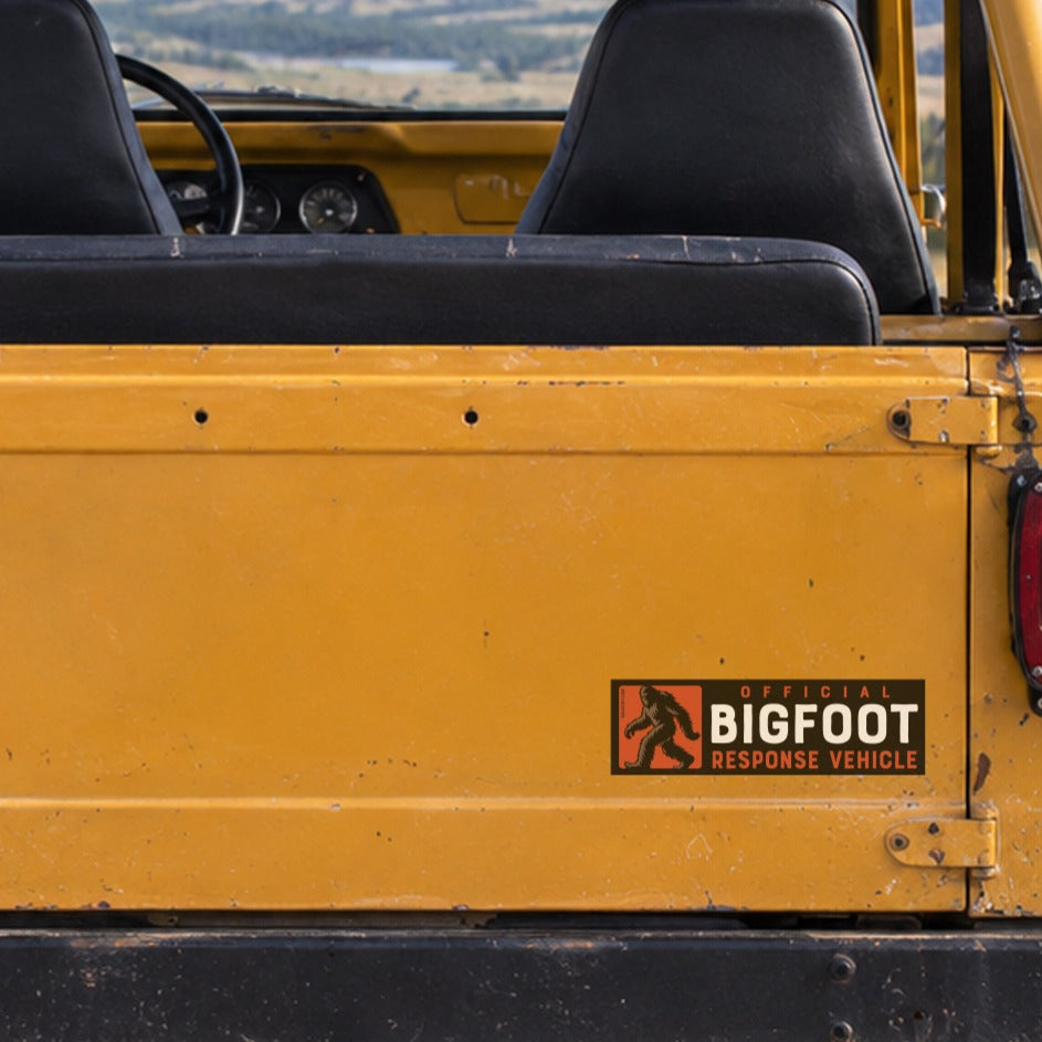On the yellow tailgate of an old Jeep, the Bigfoot Response Vehicle sticker sits above a Montana plate and open hills.