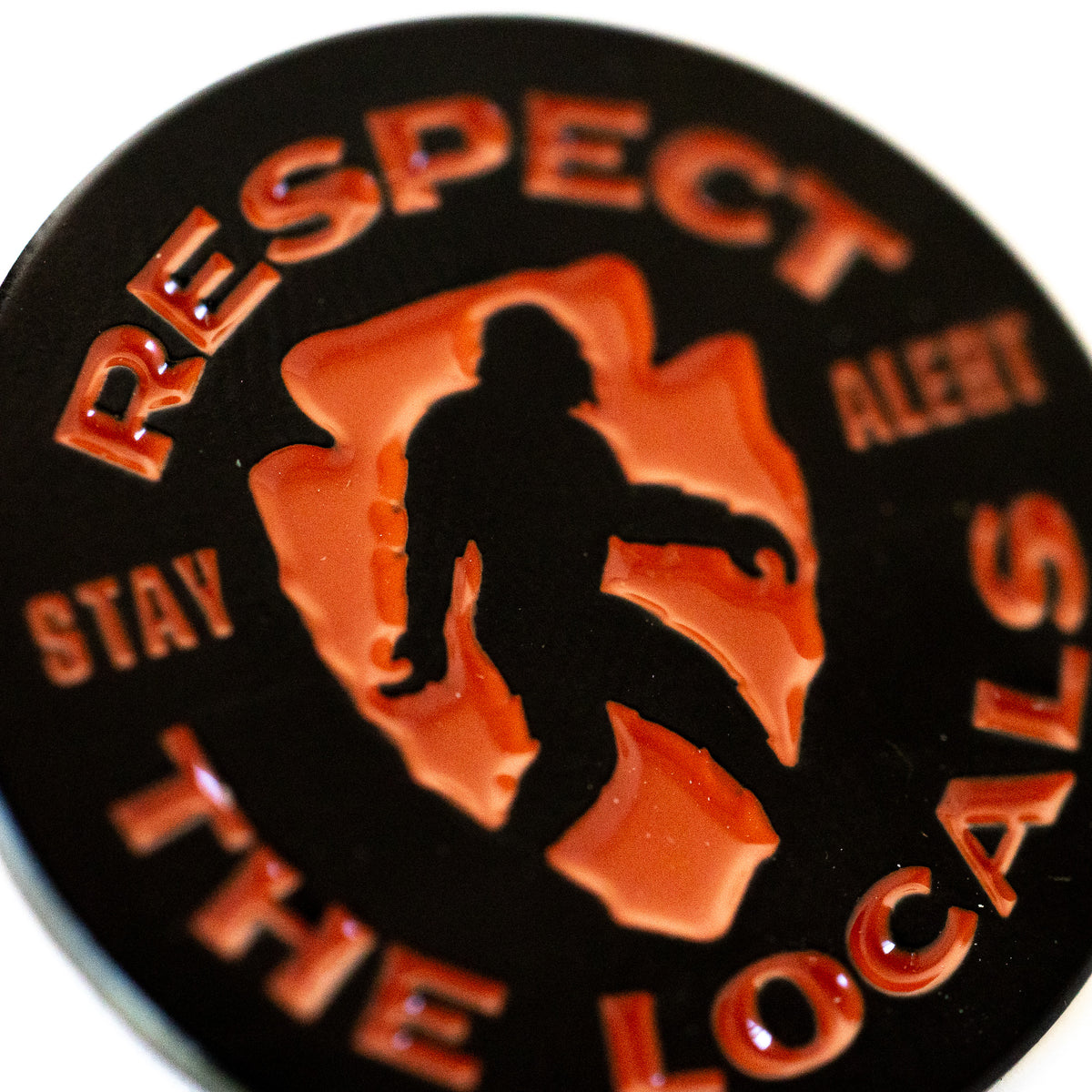 A close look at the Respect The Locals pin shows the glossy orange enamel and raised black lettering in detail.
