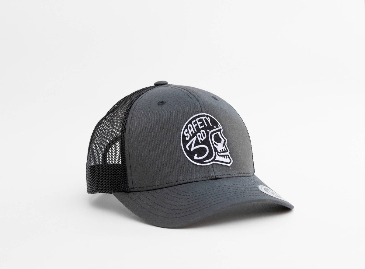 Charcoal front panels carry the Safety 3rd Helmet trucker hat patch, with black mesh sides against a white backdrop.