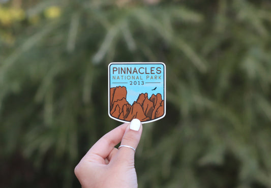 Farther back against soft pine branches, the Pinnacles National Park sticker sits small between finger and thumb.