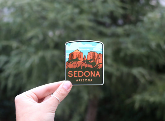 Pinched at arm's length, the Sedona Arizona sticker reads small in front of a tall pine.