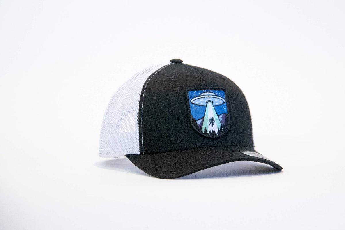 Black crown with white mesh sides on the Bigfoot UFO Conspiracy trucker hat, saucer patch centered on the front.