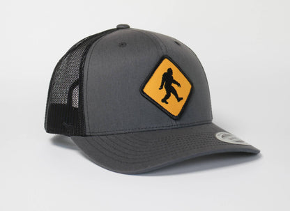 Charcoal panels meet black mesh on the Bigfoot Crossing trucker hat, patch angled toward the brim.