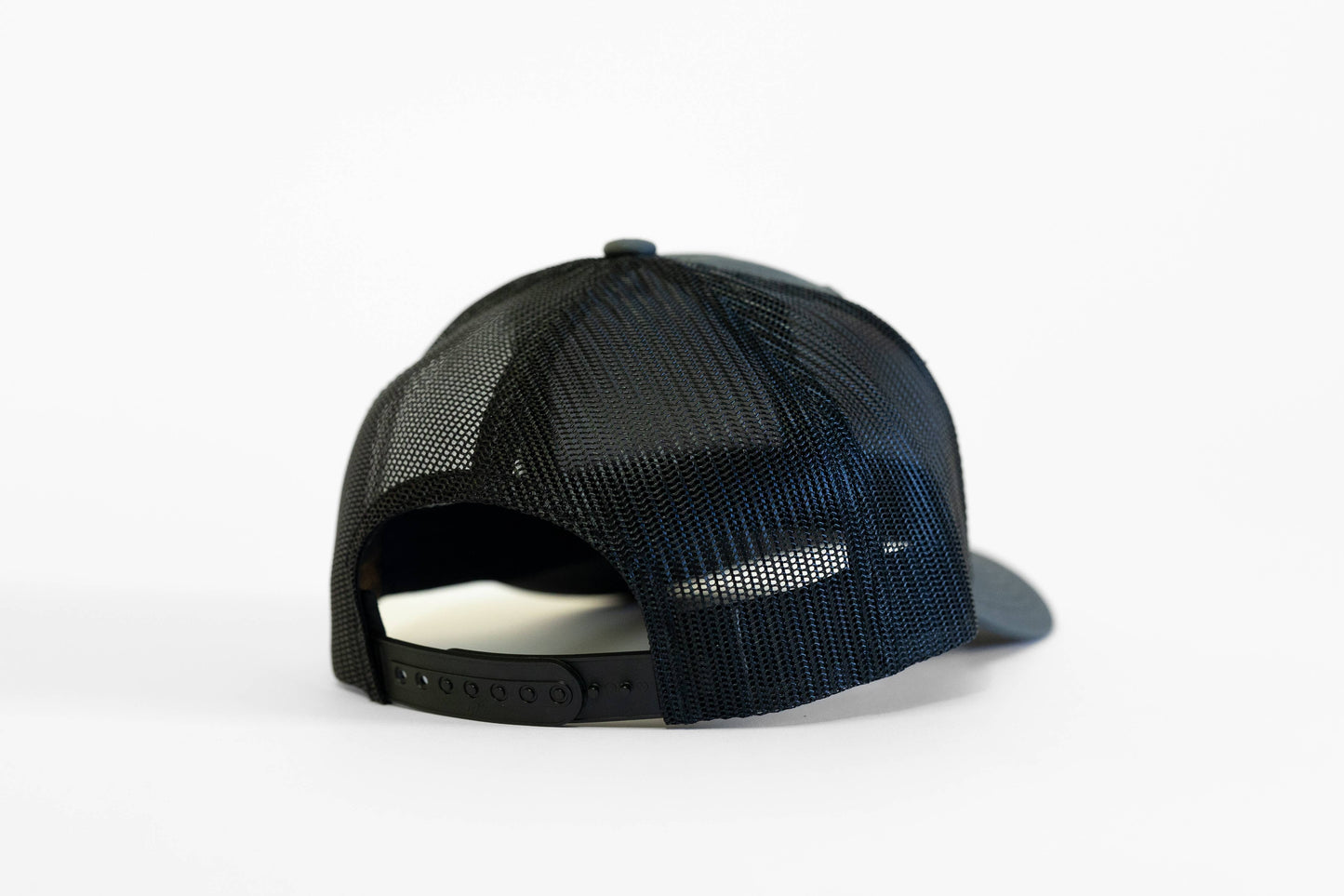 Back view of the black mesh Safety Third trucker hat with its snapback closure open above a white surface.