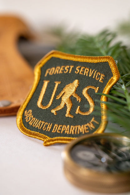 Close and angled, the US Sasquatch Department patch shows its raised gold thread with a compass edge below.