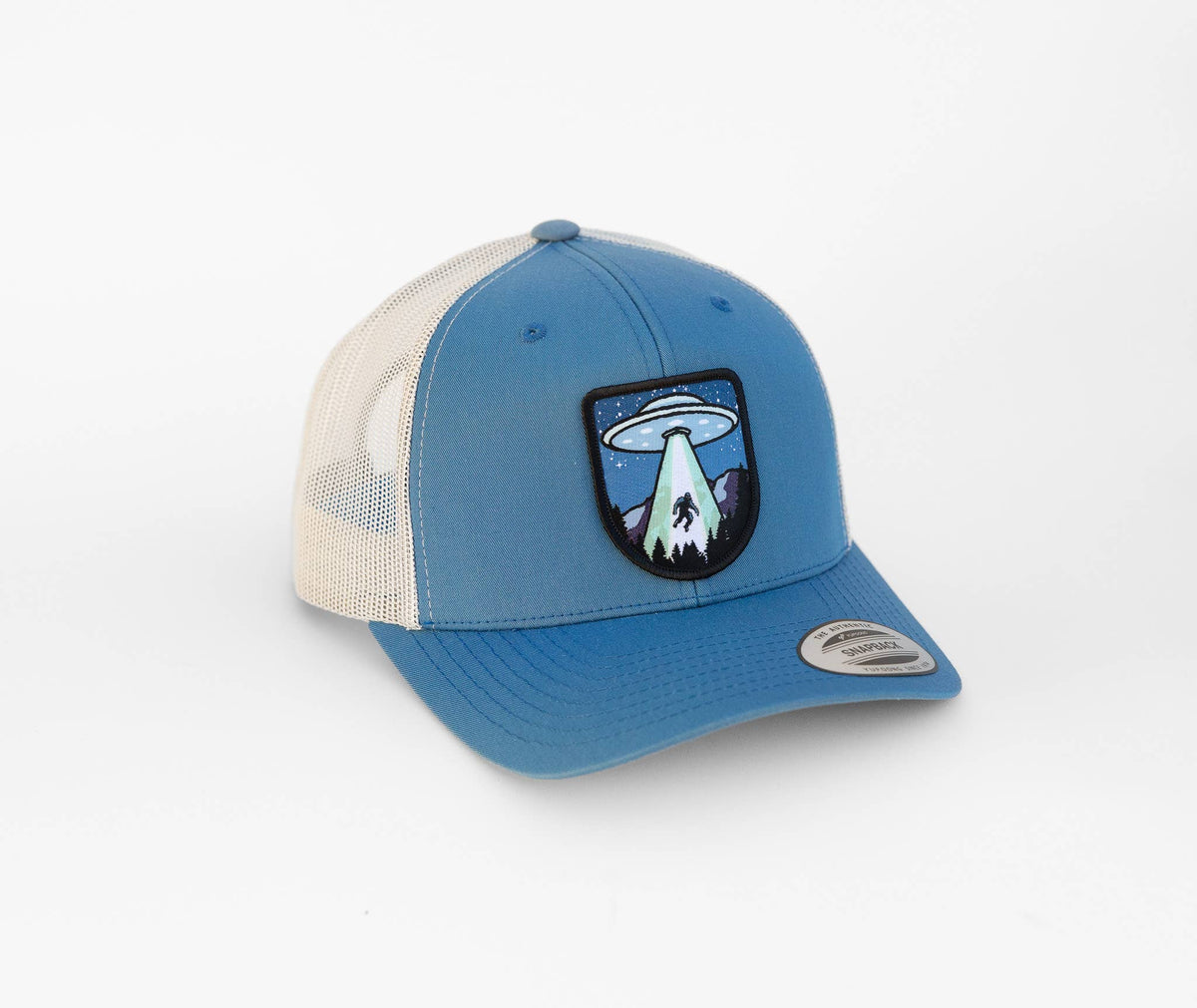 Steel blue crown and birch mesh on the Bigfoot UFO Conspiracy trucker hat, brim curved and patch facing forward.