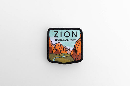 Laid flat on white, the Zion National Park woven patch shows red canyon walls and a river under black borders.