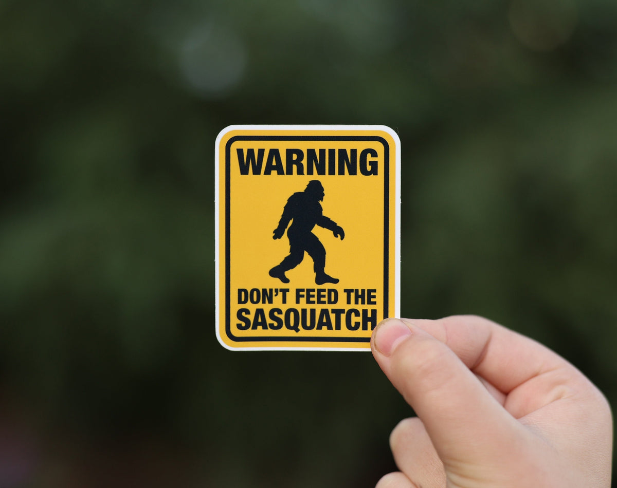 Pinched lower in the frame, the Don't Feed The Sasquatch sticker shows its black bigfoot silhouette and warning text.