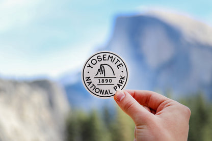 A hand lifts the Yosemite National Park B&W sticker with Half Dome rising in the haze behind it.