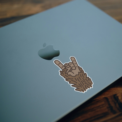 Stuck beside the logo on a pale blue laptop lid, the Bigfoot Rocks sticker sits over a wood desk.