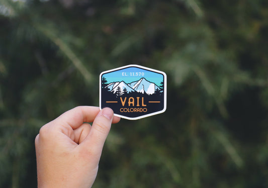 Held farther back against evergreen branches, the Vail Colorado sticker shows its full six sided badge shape.
