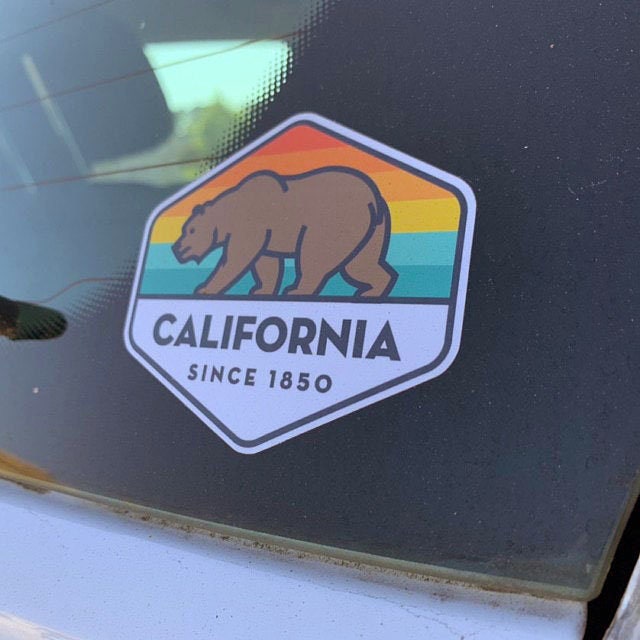 Stuck to a dusty car window, the California State Bear sticker sits above the door seal.