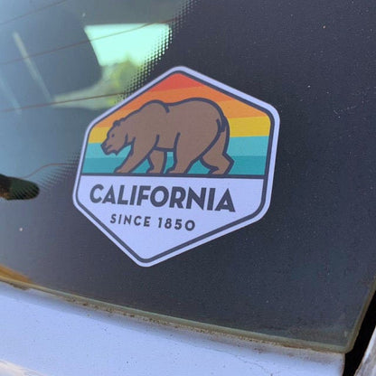 Stuck to a dusty car window, the California State Bear sticker sits above the door seal.
