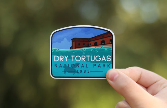 Held further back, the Dry Tortugas National Park sticker shows its full arched shape over soft leafy background.