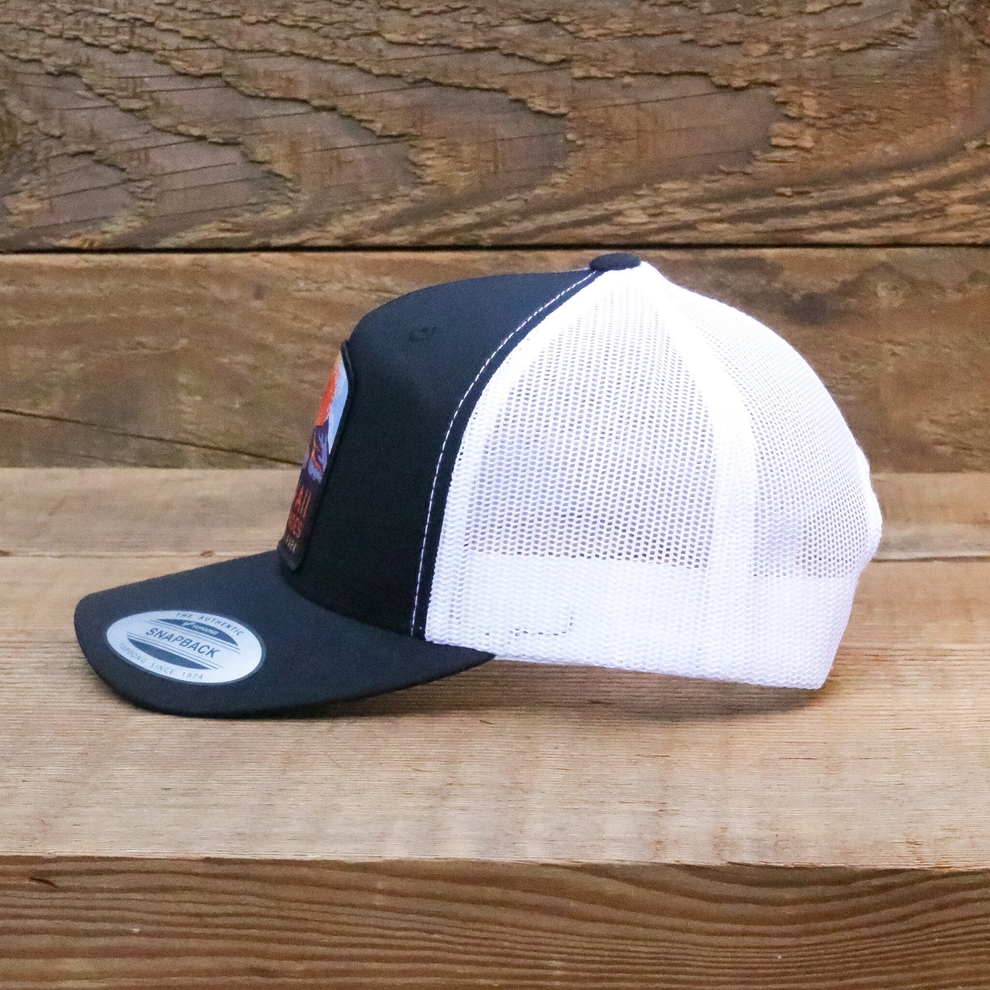 Full side profile against grey boards, white mesh and black brim on the Hawaii Volcanoes trucker hat.