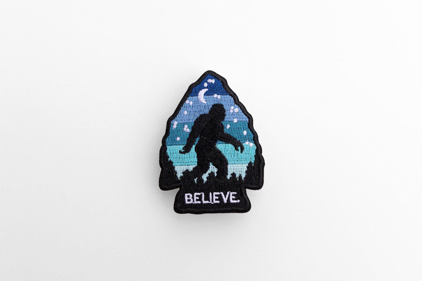 Centered on a pale grey background, the Bigfoot Believe patch shows its black merrowed border.