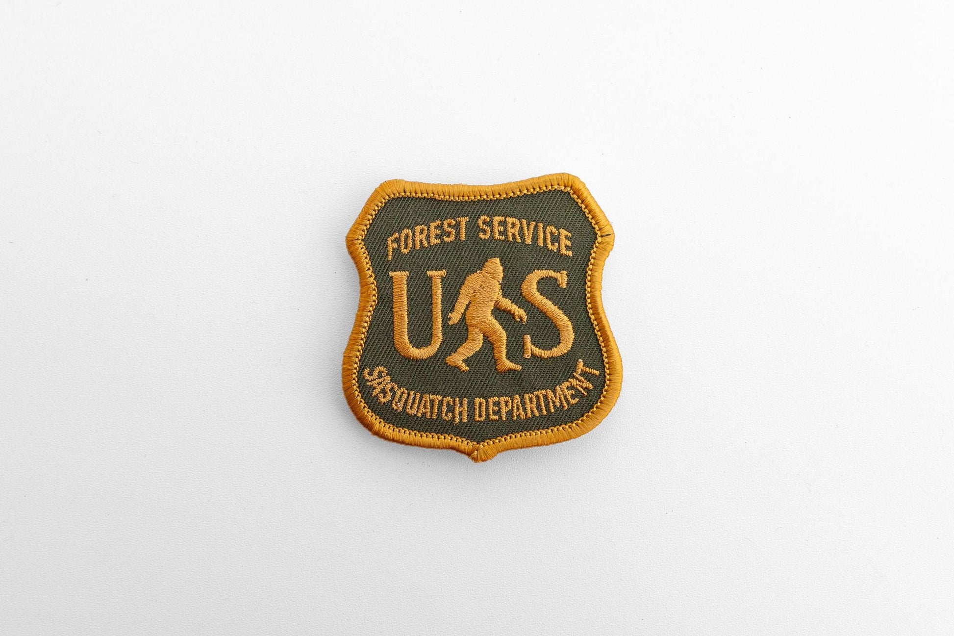Small against a plain pale backdrop, the US Sasquatch Department patch reads Forest Service across the top.