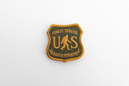 Small against a plain pale backdrop, the US Sasquatch Department patch reads Forest Service across the top.