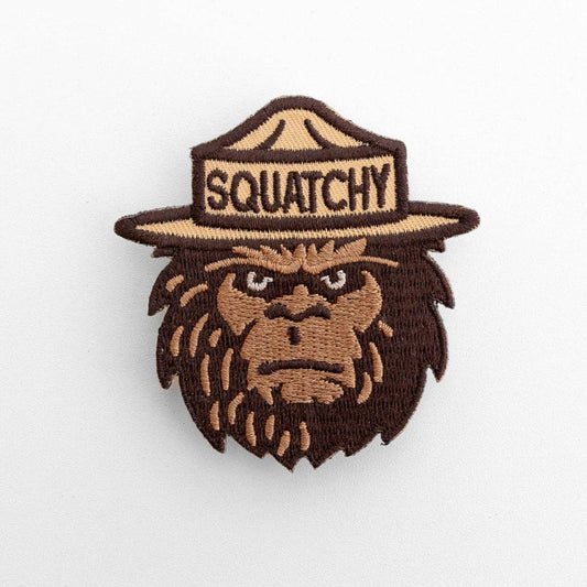 On a plain white background, the Squatchy patch shows a bigfoot face in a ranger hat stitched in browns.