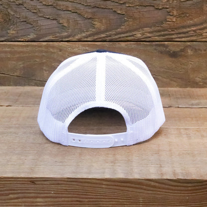 From the back on rough wood, the white mesh and plastic snapback strap of the trucker hat.