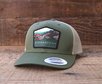 Turned slightly left against barn wood, the Shenandoah National Park trucker hat shows ridges and trees on the patch.