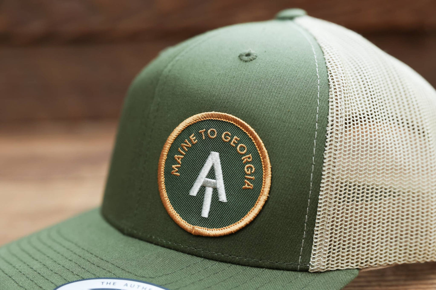 Tight crop on green twill where the Maine to Georgia patch curves toward the cream mesh side panel.
