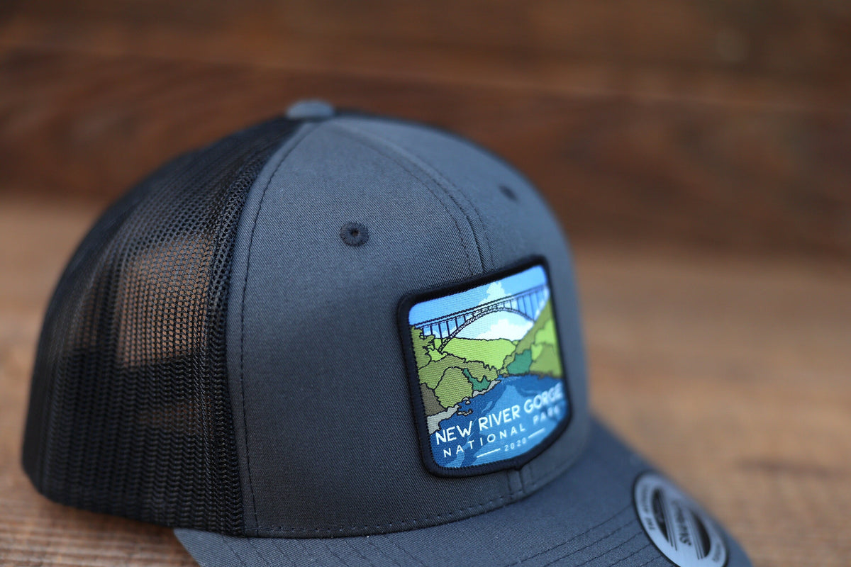 Stitched to the front of a grey and black trucker hat, the New River Gorge National Park patch catches the light.