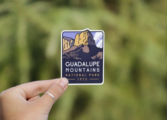 Held farther back in wider framing, the Guadalupe Mountains National Park sticker shows its peak and 1972 date.