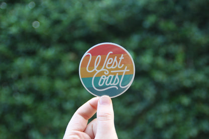 Held a little farther back against dark leaves, the West Coast Life sticker catches soft daylight.