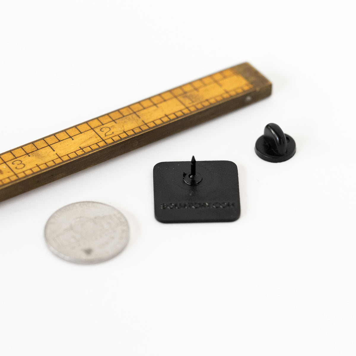 Flipped over beside a ruler and a coin, the Bigfoot Crossing pin shows its post, clutch, and stamped backside.