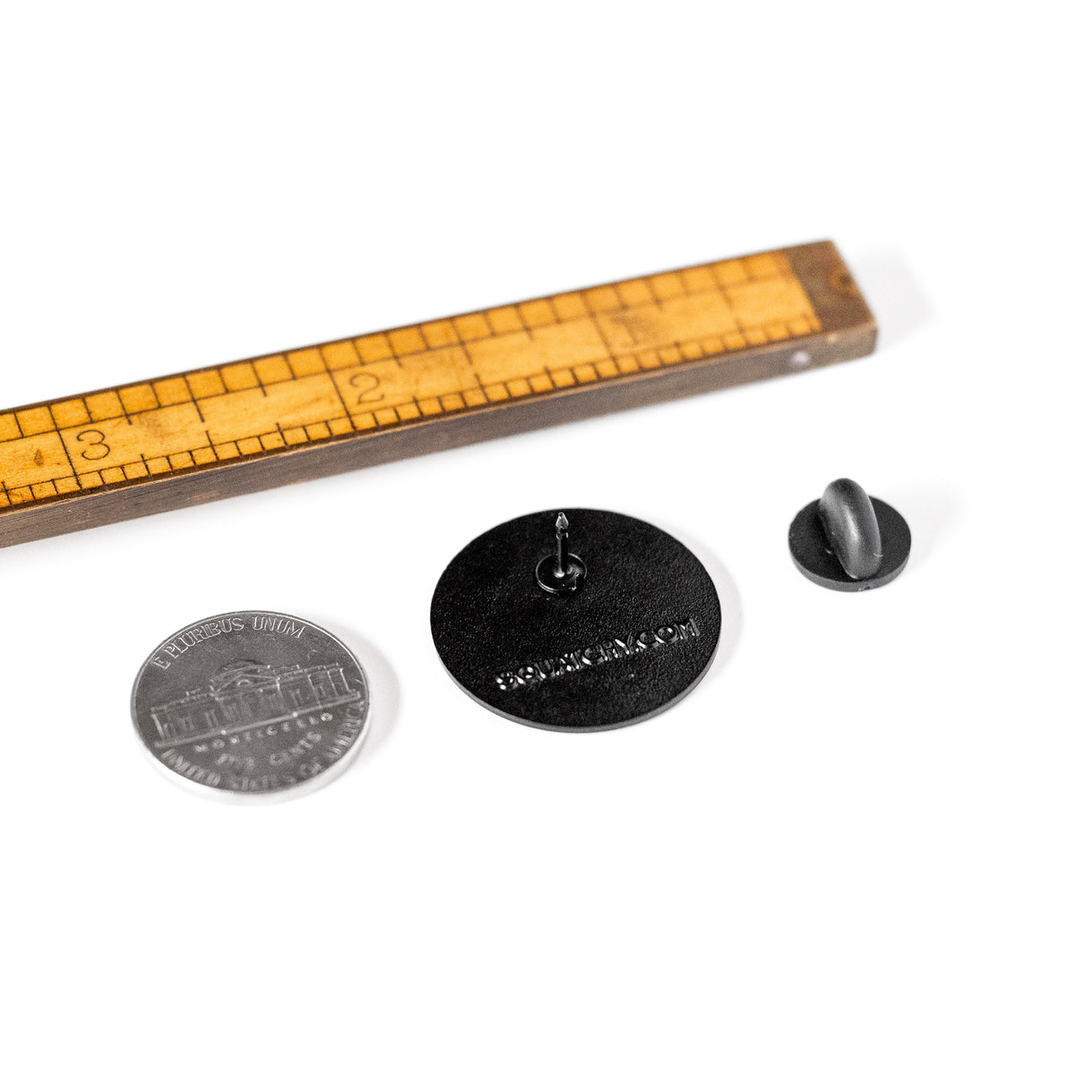 Flipped over beside a ruler and a nickel for scale, the Respect The Locals pin reveals its rubber clasp backing.