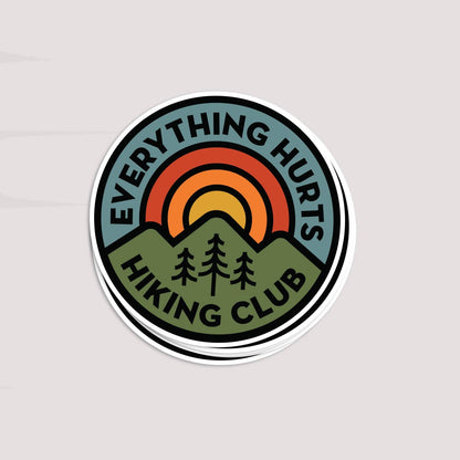 Tilted on a pale grey backdrop, a small stack of Everything Hurts Hiking Club stickers casts a soft shadow.