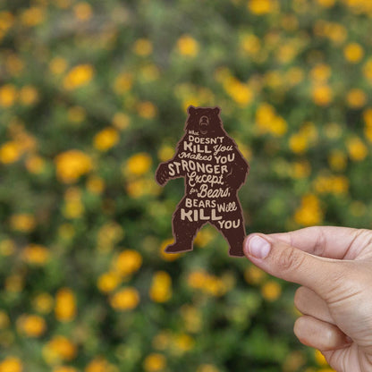Yellow wildflowers blur behind the Bears Will Kill You sticker held by one hand.