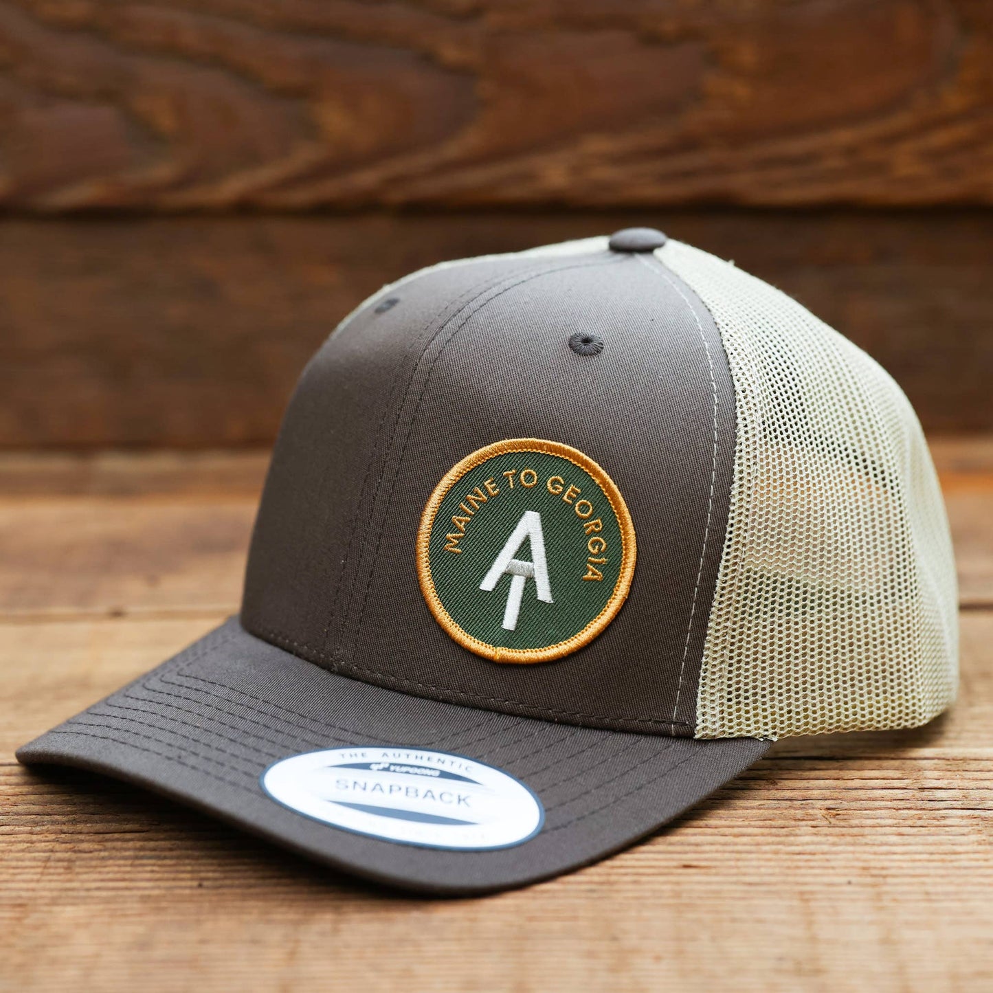 Set on weathered planks, the brown AT Maine to Georgia trucker hat still wears its Snapback sticker.