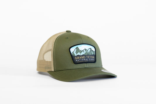 Angled against white, the olive and tan Grand Teton National Park trucker hat shows its mountain patch.