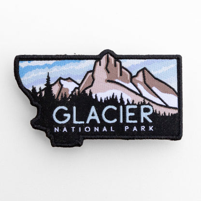 Filling the frame, the Glacier National Park patch shows snow on the ridges and a striped sky above dark firs.