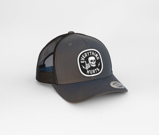 Charcoal crown with black mesh, the Everything Hurts trucker hat turns to show its round skull patch.