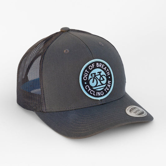 Charcoal Out of Breath Cycling Team trucker hat turned to show its round blue bicycle patch and dark mesh side.