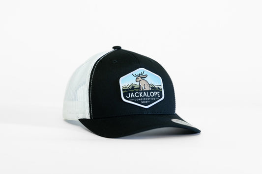 Black and white Jackalope Conservation Society trucker hat angled on a plain white backdrop, patch facing forward.